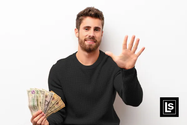 Business owner holds up 5 fingers of one hand while holding a stack of money in the other